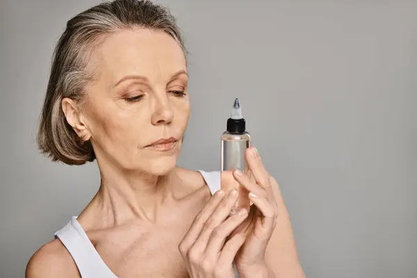 stock image A mature woman gracefully holds a skin care product bottle.