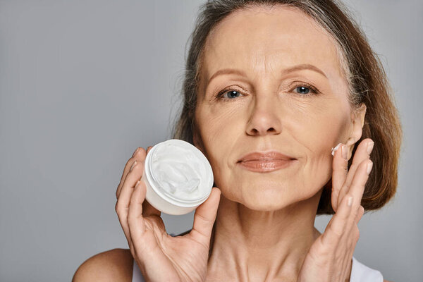 Женщина усиливает свою красоту, нанося крем на лицо.