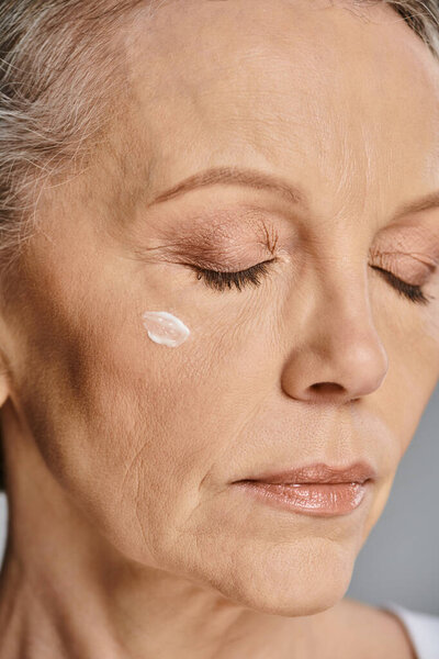 A mature woman applying cream on her face for a rejuvenating skincare routine.