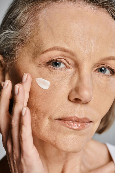 An elegant older woman gently applying cream to her face, taking care of her skin.