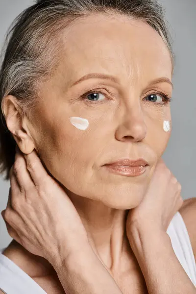 stock image A mature, attractive woman in comfy attire applying cream to her face.