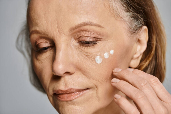 A mature woman applies cream to her face, enhancing her natural beauty.