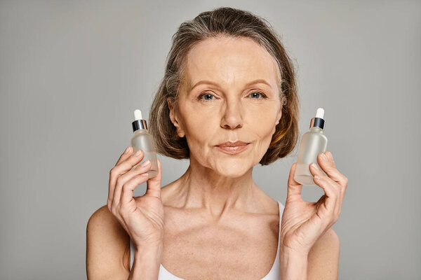 A mature, attractive woman elegantly holds two bottles of skin care products.