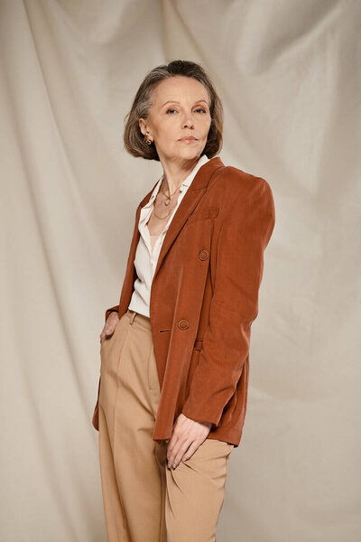 A mature woman in a brown blazer and tan pants, exuding confidence and style, engages in active poses.