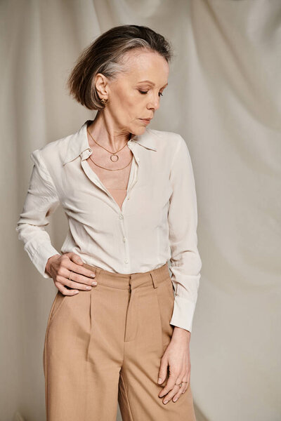 Mature woman in white shirt and tan trousers, engaged in graceful posing.