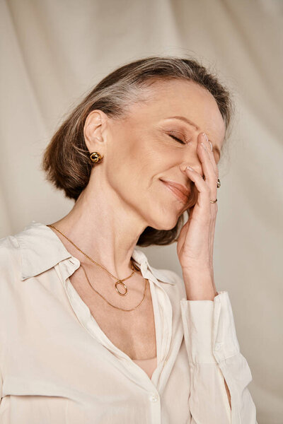 Mature woman in cozy attire covering her face with hands.