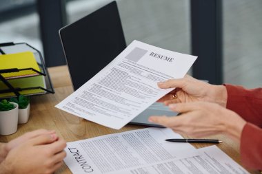 A man hands a resume to a woman at a desk. clipart