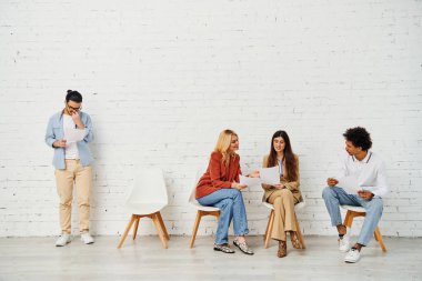 Beyaz bir duvarın önünde sandalyede oturan bir grup çekici insan..