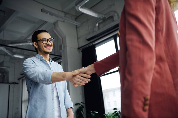 Мужчина и женщина в офисной обстановке, сердечно пожимающие руки.