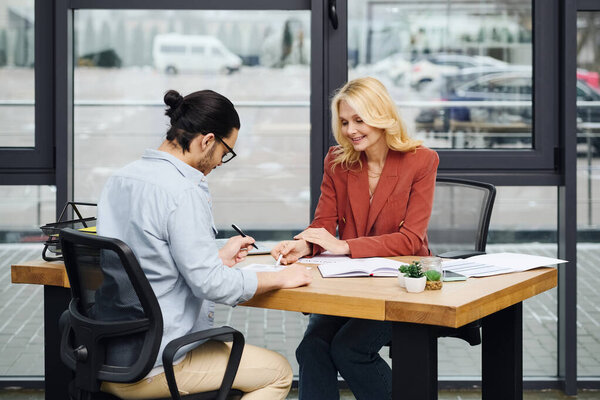 A man and woman engaged in a conversation at a desk in an office.