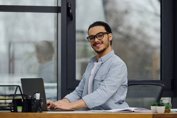 A man focuses on his laptop while sitting at a desk.