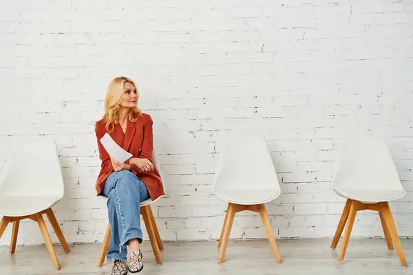 stock image A stylish woman sitting on a chair in front of a textured brick wall.