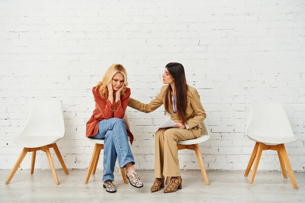 Two elegant women engaged in deep conversation while seated in chairs.