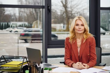 A woman sits focused at a desk in a modern office setting. clipart