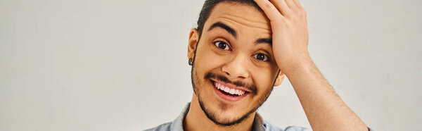 A man smiling happily at camera, hand on head.