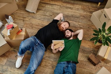 A couple of men laying peacefully on a wooden floor in their new home, a moment of rest amidst the moving boxes. clipart