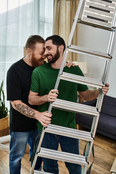 Two men, part of a gay couple, stand side by side near a ladder, in their new home.