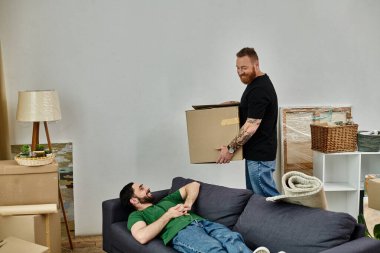 Oturma odasındaki bir kanepede rahatça uzanan bir adam, hayatında yeni bir sayfa açmanın heyecanı içinde kutuları taşırken..