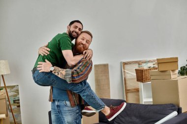 Taşınan kutularla dolu bir odada kucaklaşan iki adam, birbirlerine aşık eşcinsel bir çift olarak hayatlarında yeni bir bölümü sembolize ediyorlar..