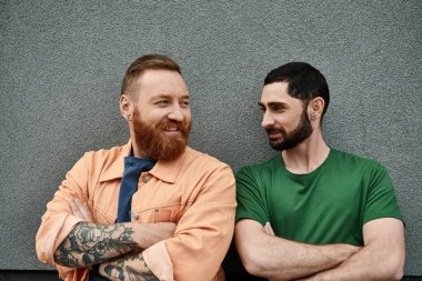 Gri duvarın önünde dikilen ve aşk ve beraberlik saçan gündelik kıyafetler giyen eşcinsel çift..