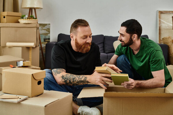 Two happy men, a gay couple in love, sit atop boxes in their new home, embracing their fresh start with joy.