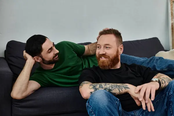 stock image A gay couple shares a tender moment as they sit closely on top of a couch, surrounded by moving boxes in their new home.