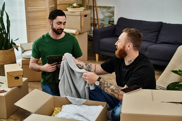 A gay couple embraces lovingly while sitting on the floor surrounded by moving boxes in their new home.
