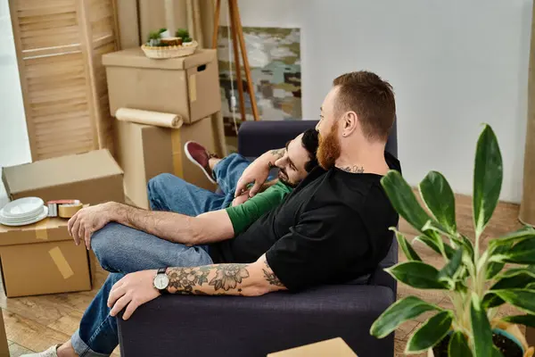 stock image A gay couple sits on a cozy couch in their new living room, surrounded by moving boxes, symbolizing love and new beginnings.