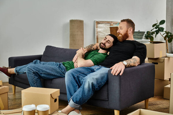 Влюблённые геи сидят на диване, окружённые коробками и начинают новую главу в своём жизненном путешествии..