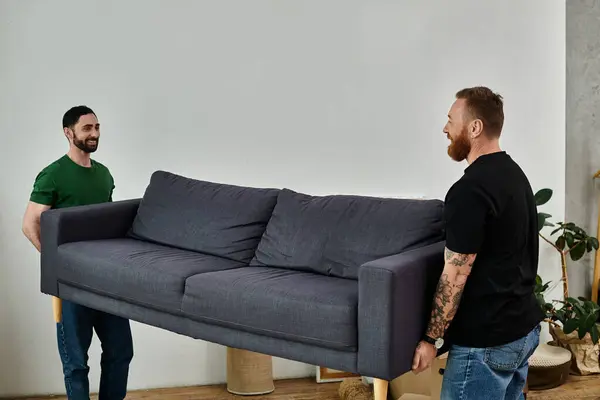 stock image A man carrying sleek gray couch in a new home, beginning a fresh chapter in life.