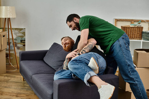 gay couple lays on a couch in a moment of fun and relaxation, amidst boxes in a new home.