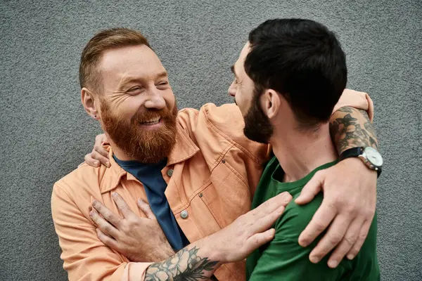 stock image A portrait of a gay couple in love, wearing casual attire, embracing each other in front of a grey wall.