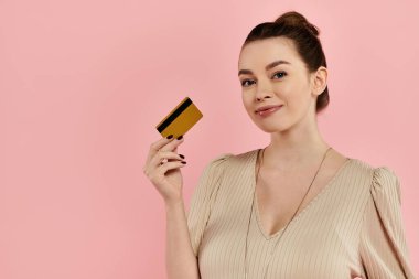 A pregnant woman elegantly holds a credit card in her hand against a pink backdrop. clipart