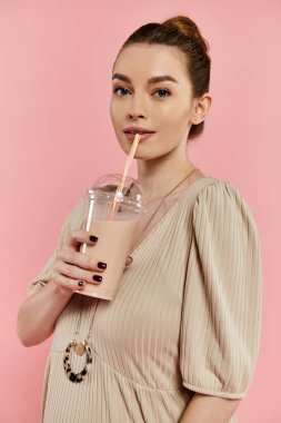 A young pregnant woman in a flowing dress delicately holds a drink in a serene gesture, set against a pink backdrop. clipart