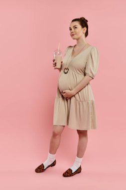 Pembe arka planda elinde milkshake tutan hamile bir kadın..