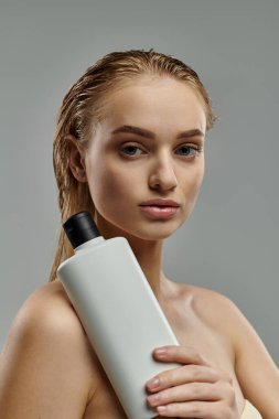 Genç bir kadın elinde bir şişe şampuan tutarak saç bakımını gösteriyor..