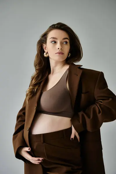stock image A stylish young pregnant woman in a brown suit striking a pose on a grey background.
