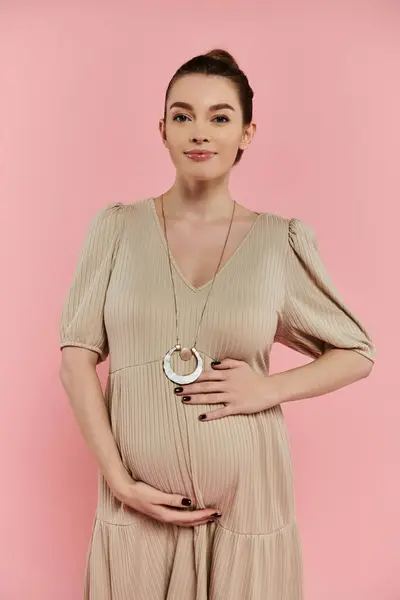 stock image A young pregnant woman in a flowing dress poses elegantly for a shot against a vibrant pink backdrop.