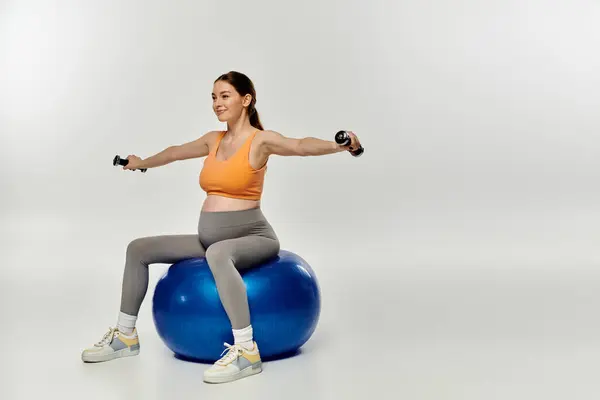 stock image A pregnant woman in athletic attire sits on a stability ball while holding a dumbbell.