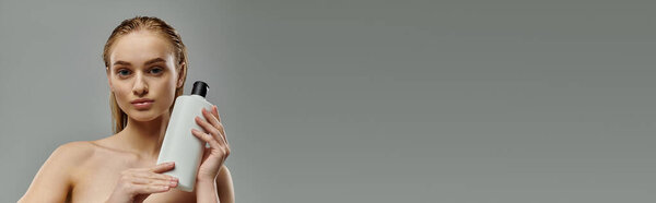 Привлекательная женщина чувственно держит бутылку лечения волос.