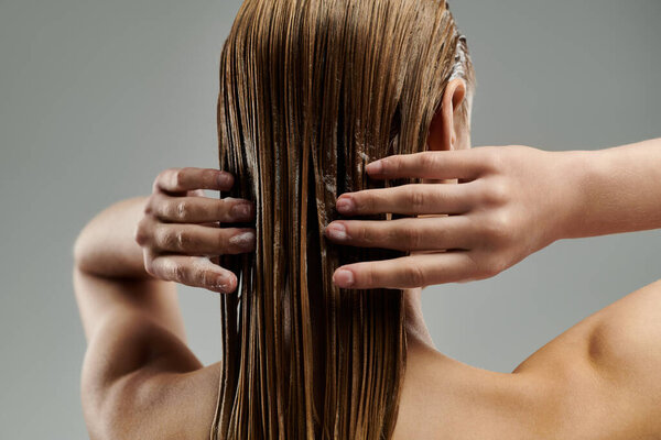 Молодая женщина изящно удерживает влажные волосы руками.