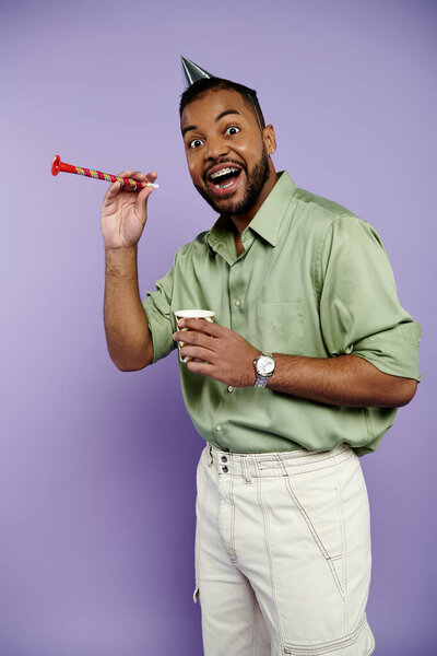 Молодой афроамериканец в брекетах радостно держит соломинку, надевая шляпу на яркий фиолетовый фон..