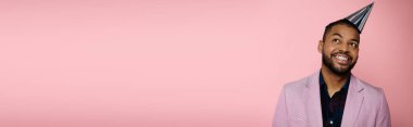 Diş telleriyle süslenmiş genç Afrikalı Amerikalı adam pembe arka planda canlı bir parti şapkası sergilerken mutluluk saçıyor..