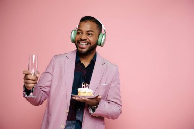 Diş telli genç Afrikalı Amerikalı adam kulaklıkla müzik dinlerken doğum günü pastası tutuyor..
