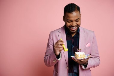Pembe takım elbiseli şık bir Afro-Amerikan erkeği canlı pembe bir arka plana karşı bir tabak pasta ve parti kornası tutuyor..