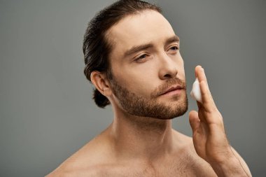 Stüdyodaki gri arka planda köpük temizleyici uygulayan yakışıklı bir adam..