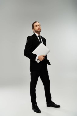 A bearded businessman in a sharp suit holds a crucial document, exuding confidence and professionalism against a grey backdrop. clipart