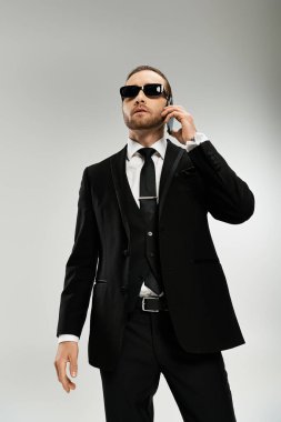 Parlak takım elbiseli ve güneş gözlüklü sakallı bir işadamı cep telefonuyla konuşuyor, özgüven ve profesyonellik yayıyor..