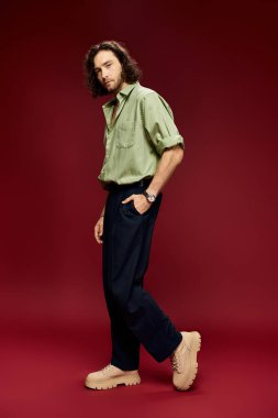 Gözlüklü ve yeşil ipek gömlekli yakışıklı bir adam kırmızı arka planda poz veriyor..