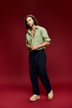 Gözlüklü ve yeşil ipek gömlekli yakışıklı adam kırmızı arka planda güvenle poz veriyor..